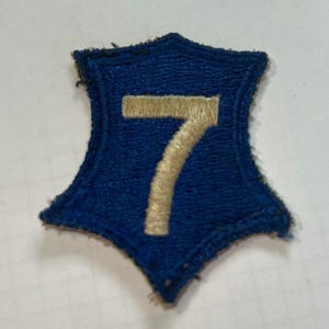 May include: A blue felt patch with a white embroidered number 7 in the center. The patch is shaped like a five-pointed star.