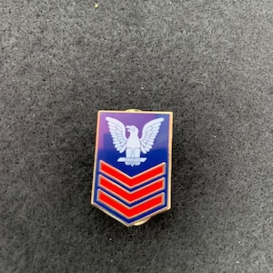 May include: A blue and red military rank pin with a white eagle and three red stripes.