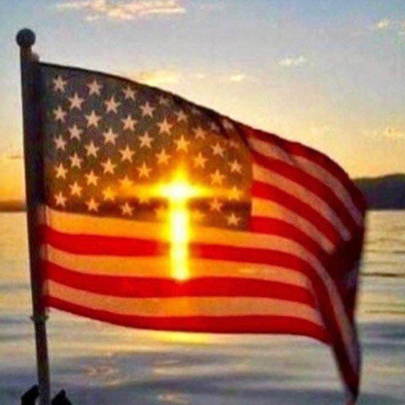K&ouml;nnte beinhalten: Die amerikanische Flagge weht im Wind, mit der Sonne, die durch die Mitte in Form eines Kreuzes scheint. Die Flagge hat rote und wei&szlig;e Streifen und ein Feld wei&szlig;er Sterne auf blauem Grund. Der Hintergrund ist ein Sonnenuntergang &uuml;ber dem Wasser.