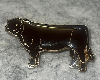 Op de afbeelding: Een zwarte emaille reversspeld in de vorm van een stier, voorzien van goudkleurige metalen omlijningen die het gespierde silhouet, de kop en de poten van het dier definiëren. Het ontwerp toont de stier in profiel met gepolijste zwarte vlakken.