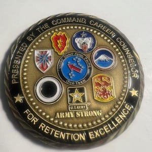 May include: A gold-colored coin with a black border and a star on each side. The coin features the text "Presented by the Command, Career Counselor for Retention Excellence" around the edge. The center of the coin features a variety of military insignia, including the United States Army logo, and the text "Army Strong".