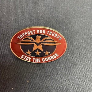 May include: A red, white, and gold pin with an eagle and three stars. The pin says "Support Our Troops Stay The Course".