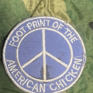 May include: A blue and white embroidered patch with a peace sign and the text "Foot Print of the American Chicken".