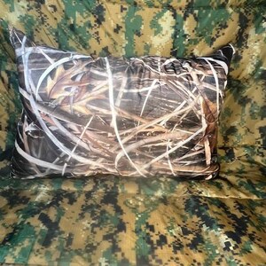 May include: A brown and tan camouflage pillow with a pattern of leaves and branches.