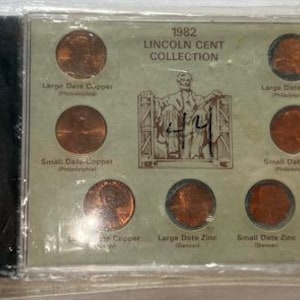 May include: A 1982 Lincoln Cent Collection in a clear plastic case. The display includes several copper and zinc pennies, with text indicating large and small date variations. The case also features an image of Abraham Lincoln.