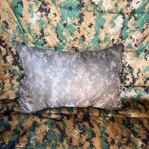May include: A camouflage-patterned pillow with a light gray background and dark green, brown, and black spots. The pillow is made of a soft, comfortable material and is perfect for adding a touch of style to any room.