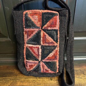 Op de afbeelding: Een zwarte stoffen handtas met een bruin en zwart geometrisch patroon aan de voorkant. De tas heeft een lange schouderband.