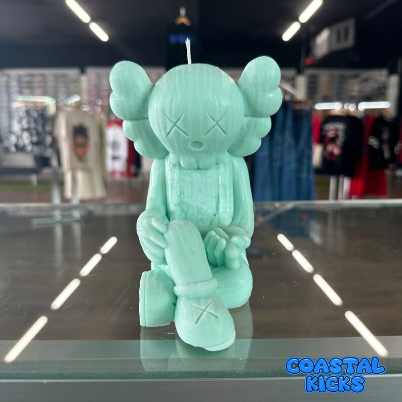 May include: A light green candle shaped like a cartoon character with X eyes and a sitting pose.