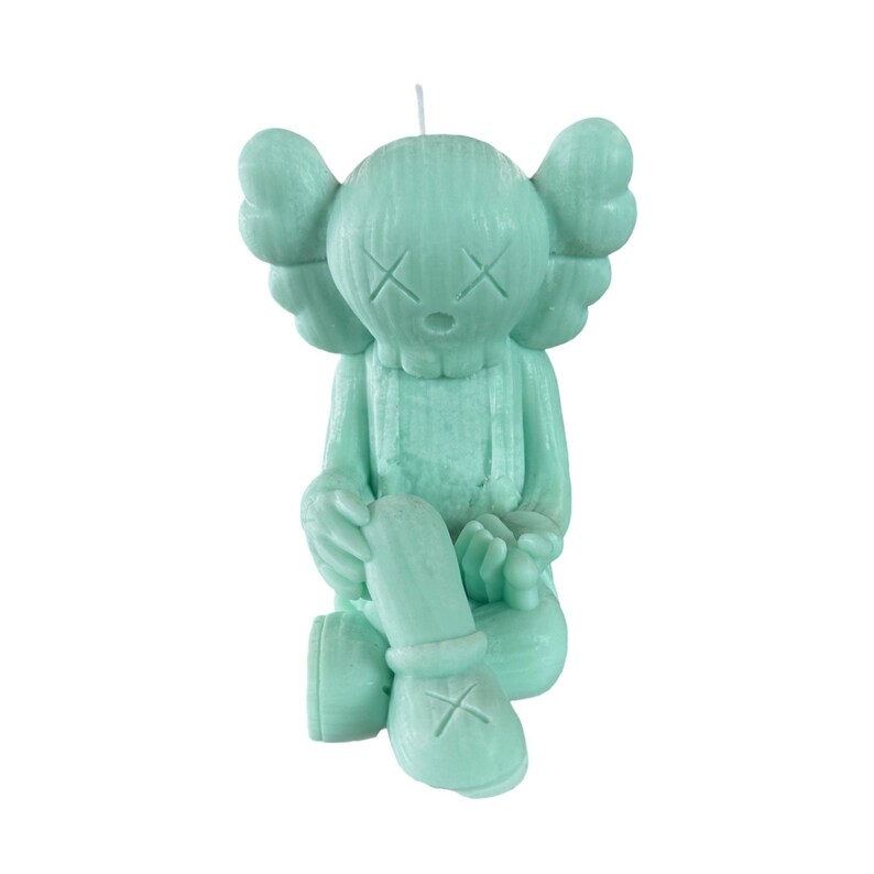 May include: A green candle shaped like a sitting figure with large ears and a simple face. The candle has a textured surface and a small wick on top.