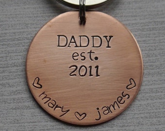 May include: Copper keychain with a round tag that says "Daddy est. 2011" with hearts and the names "mary" and "james" engraved around the edge.