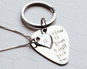 May include: Silver guitar pick necklace with a small heart charm engraved with the number 11. The pick is engraved with the text "After 11 years I still pick you".