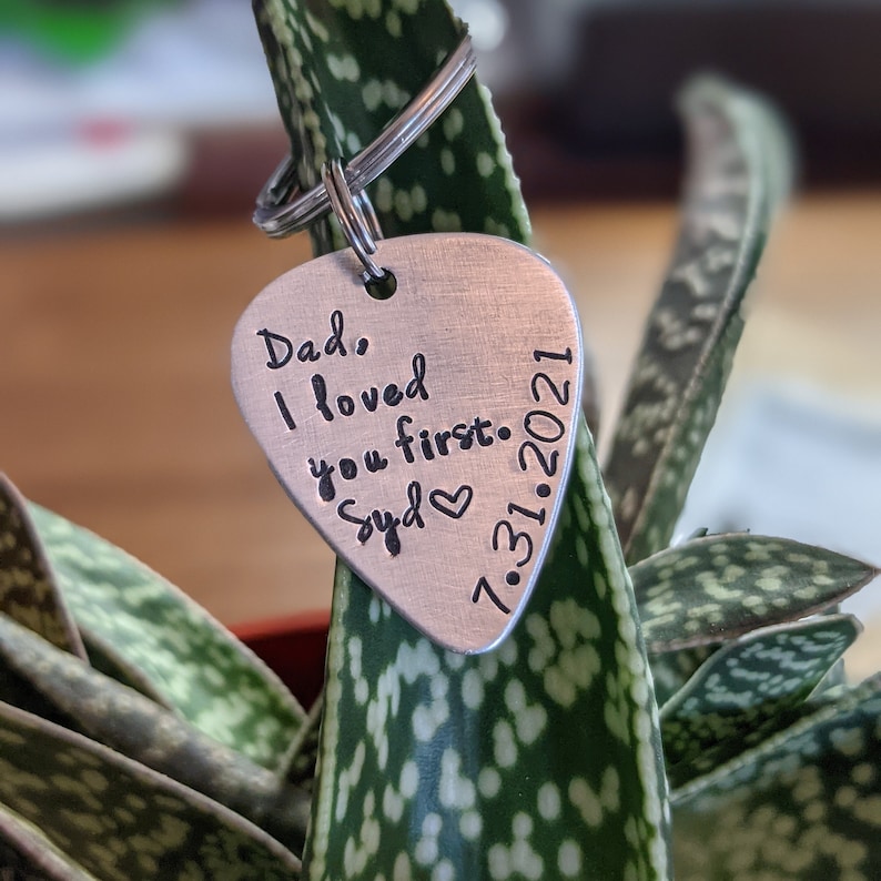 May include: Silver guitar pick keychain with the text "Dad, I loved you first. Syd" and the date "7.31.2021" engraved on it.