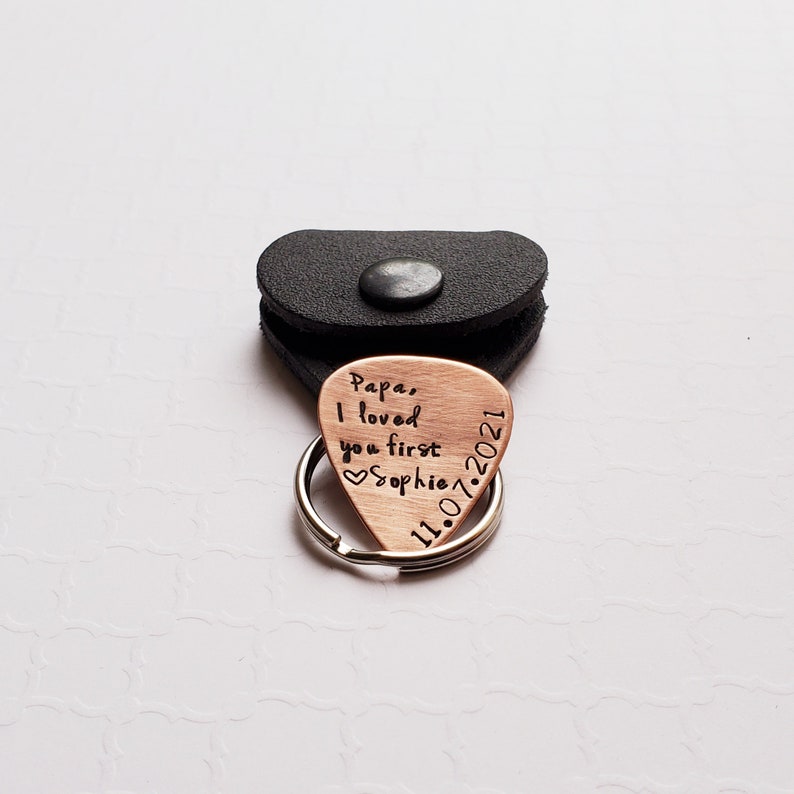 May include: Copper guitar pick keychain with the inscription "Papa, I loved you first  Sophie 11.07.2021" and a heart symbol.