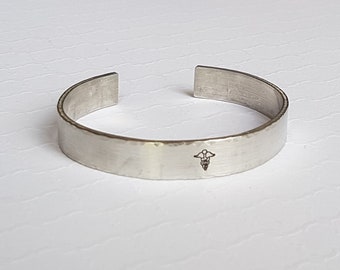 May include: Silver hammered metal bracelet with a medical symbol engraved on the front.