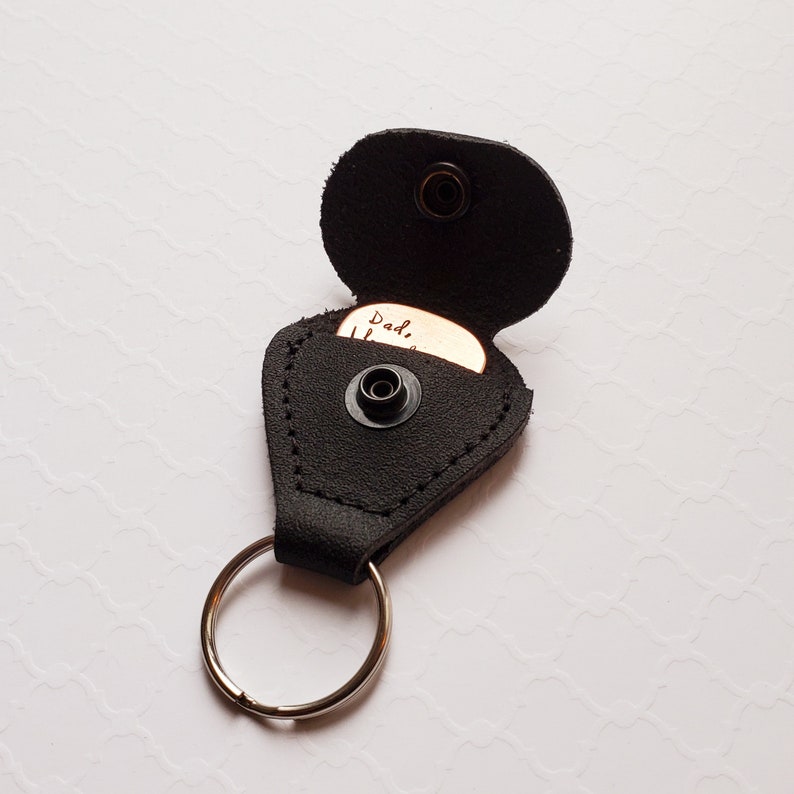 May include: Black leather guitar pick holder with a keyring. The pick is copper and engraved with the words "Dad, I love you".