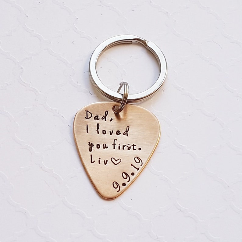 May include: Gold-colored guitar pick keychain with the text "Dad, I loved you first. Liv 9.9.19" engraved on it.