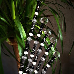 May include: Decorative beaded stems with clear crystal ball toppers. The stems feature a mix of black, white, and clear beads. The stems are arranged in front of a green leafy plant.