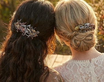 May include: Two people with their backs to the camera, each wearing a decorative hair clip. One clip is silver and gold with a dragon design, the other is gold with a floral design. The person on the left has dark hair, and the person on the right has blonde hair.