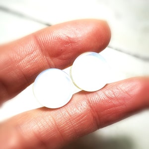 May include: Two iridescent white opal plugs, one slightly larger than the other, are held in a hand.