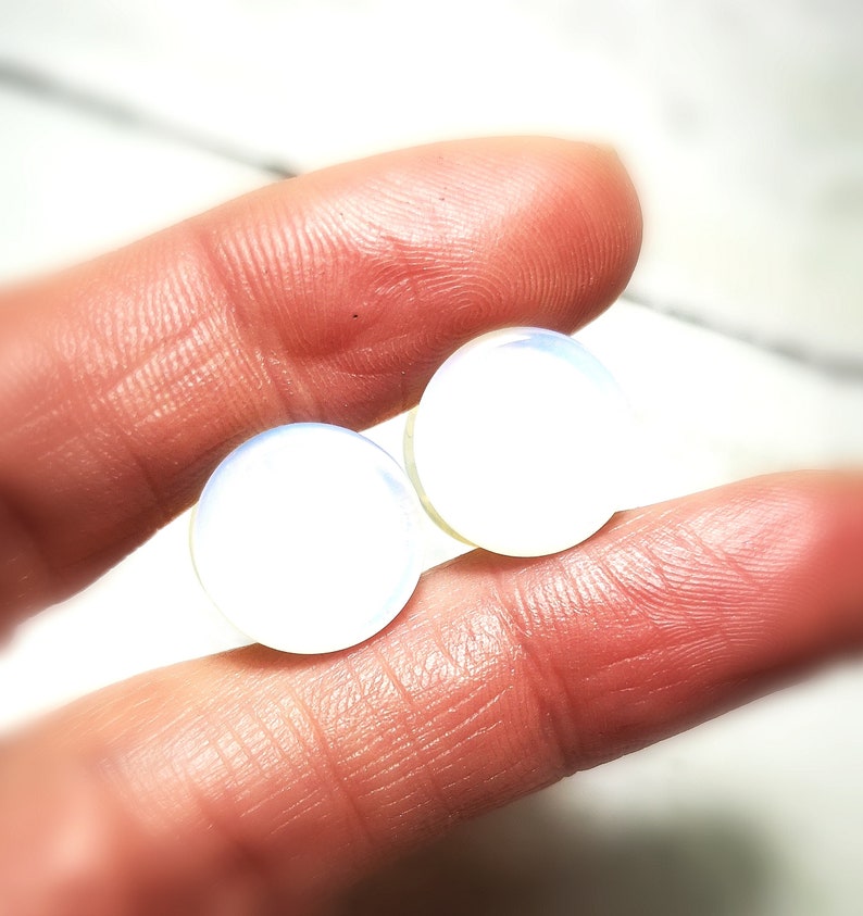 May include: Two iridescent white opal plugs, one slightly larger than the other, are held in a hand.