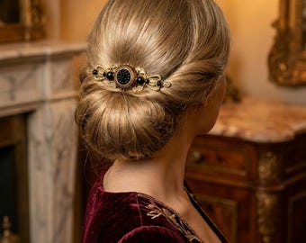 May include: A gold-toned hair comb with a central black circular design and black bead accents. The comb is set in a woman's updo, with a burgundy velvet dress visible. The hair accessory adds a touch of vintage elegance.