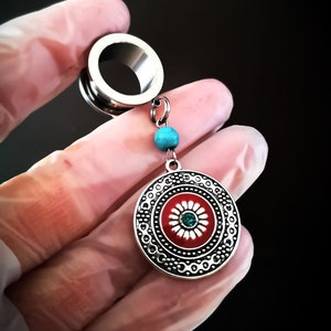 May include: Silver ear gauge with a dangling charm featuring a red and white flower with a turquoise center. The charm is attached to a silver chain with a turquoise bead.