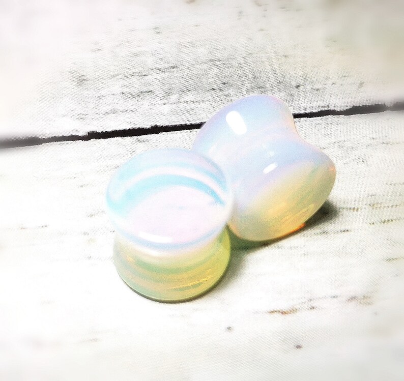 May include: Pair of iridescent white opal ear gauges. The gauges are round and have a smooth, polished finish.
