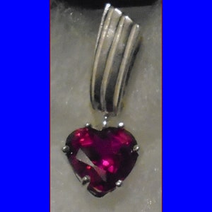 Puede incluir: Un colgante de plata con una piedra preciosa en forma de corazón de rubí.