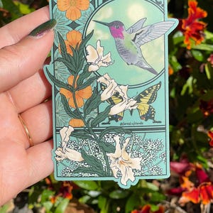 May include: A rectangular sticker with a light green background featuring the text PLANT NATIVE at the top. The design includes a pink-throated hummingbird in flight, a yellow and black butterfly, orange flowers, and white blossoms.