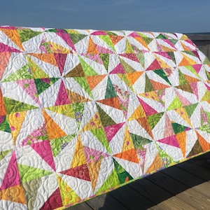 May include: A colorful quilt with a white background and a swirling pattern. The quilt is made of various fabrics in shades of pink, green, orange, and yellow.