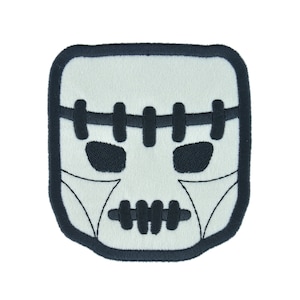 May include: A black and white embroidered patch of a Frankenstein monster's face. The patch has a white background and black stitching for the eyes, mouth, and stitches across the forehead.