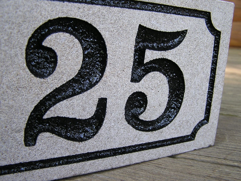 May include: A white stone house number plaque with black painted numbers "25" in a decorative font.