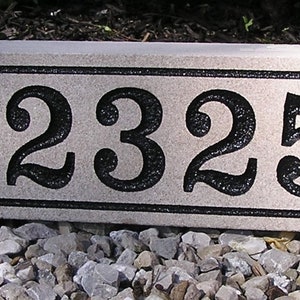 May include: A rectangular, light gray granite house number plaque with black numbers and a black border. The numbers are 12325.