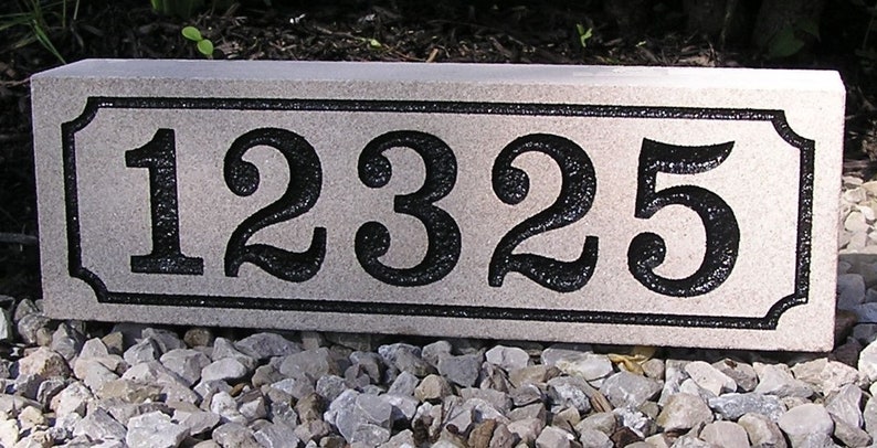 May include: A rectangular, light gray granite house number plaque with black numbers and a black border. The numbers are 12325.