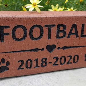 May include: A red brick engraved with the word "FOOTBALL" and a heart symbol. The brick also includes the dates "2018-2020" and two paw prints.