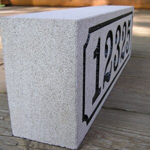 May include: A gray concrete house number block with black painted numbers "12325" on a white background.