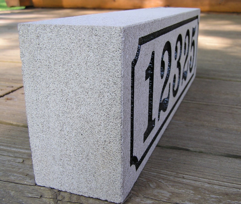 May include: A gray concrete house number block with black painted numbers "12325" on a white background.
