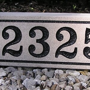 May include: A rectangular, light gray granite house number plaque with black numbers and a black border. The numbers are 12325.