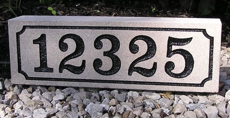 May include: A rectangular, light gray granite house number plaque with black numbers and a black border. The numbers are 12325.