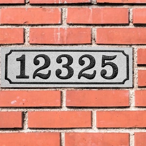 May include: A white rectangular sign with black numbers on a brick wall. The sign reads "12325".