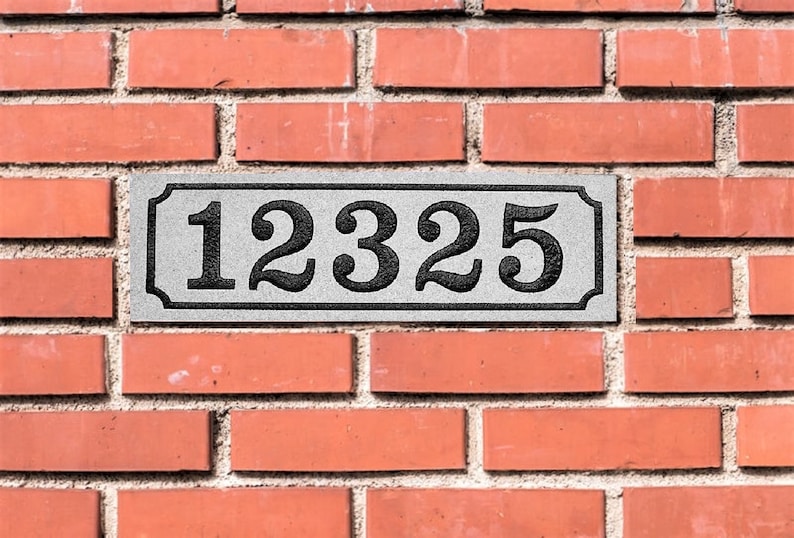 May include: A white rectangular sign with black numbers on a brick wall. The sign reads "12325".
