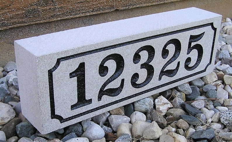 May include: A gray granite house number sign with black numbers "12325" carved into it. The sign is sitting on a bed of small gray and brown rocks.