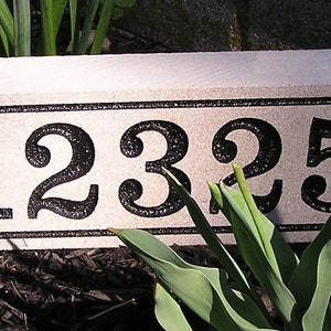 May include: A beige stone house number sign with black numbers and a black border. The numbers are 1235.