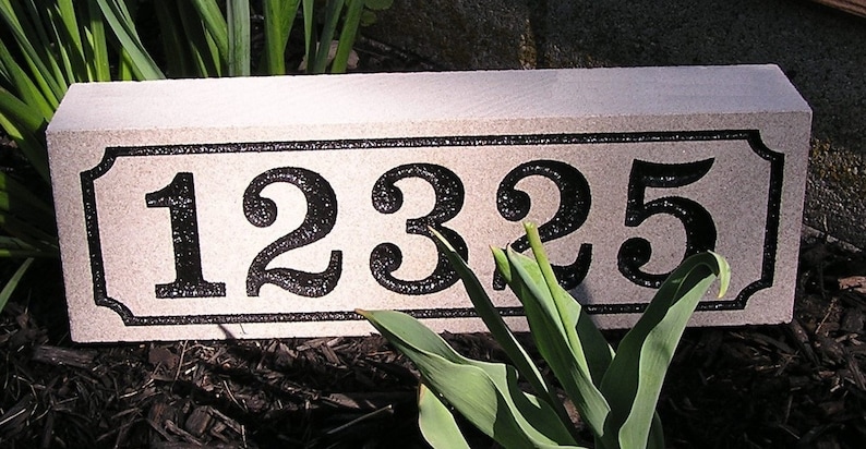May include: A beige stone house number sign with black numbers and a black border. The numbers are 1235.
