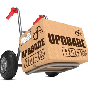 May include: A hand truck with a cardboard box labeled "UPGRADE" on top. The box has several symbols on it, including a glass, an umbrella, and an arrow pointing upwards.