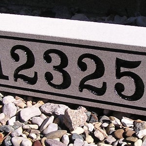 May include: A gray concrete house number plaque with black painted numbers, "12325", in a decorative font.