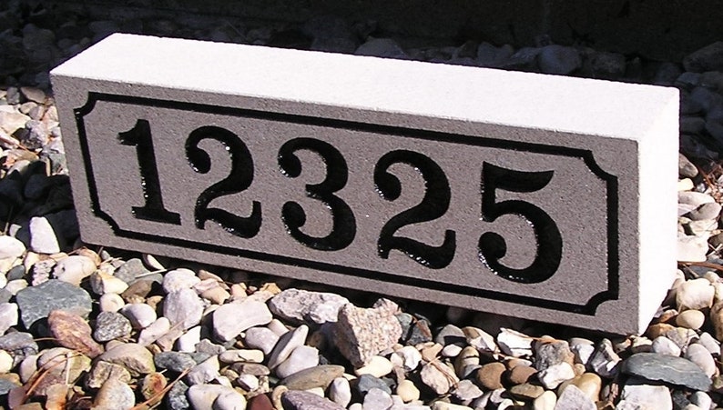 May include: A gray concrete house number plaque with black painted numbers, "12325", in a decorative font.