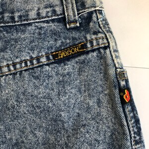 Puede incluir: Primer plano de un par de jeans de mezclilla azul claro lavados con &aacute;cido con un parche de cuero marr&oacute;n que dice "G-Star RAW" en el bolsillo trasero. Los jeans tienen un aspecto descolorido y un acabado desgastado.