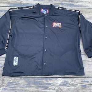 May include: Black button-up jacket with gold trim and the Philadelphia 76ers logo. The jacket features a small NBA logo patch and a Pro Player tag. The jacket is made of a smooth, athletic material.