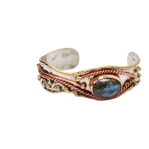 Puede incluir: Una pulsera de plata, cobre y oro con una piedra preciosa azul y verde. La pulsera tiene un diseño decorativo con alambre trenzado y pequeñas cuentas.